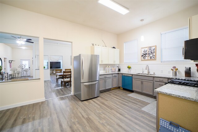 kitchen featuring appliances with stainless steel finishes, light stone countertops, light wood-type flooring, ceiling fan, and decorative light fixtures