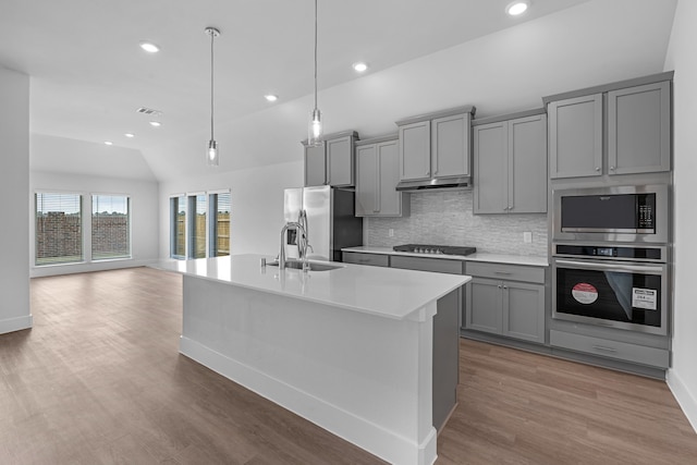 kitchen featuring light hardwood / wood-style floors, lofted ceiling, gray cabinetry, appliances with stainless steel finishes, and decorative light fixtures