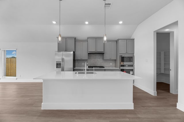 kitchen with pendant lighting, appliances with stainless steel finishes, sink, and an island with sink