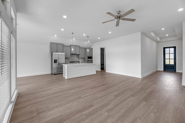 unfurnished living room with a tray ceiling, sink, ceiling fan, and light hardwood / wood-style flooring