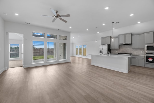 kitchen with light hardwood / wood-style floors, appliances with stainless steel finishes, decorative light fixtures, a kitchen island with sink, and gray cabinets