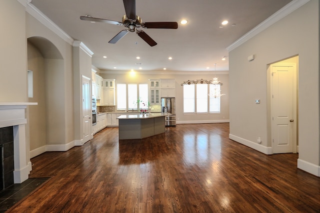 unfurnished living room with ceiling fan with notable chandelier, ornamental molding, a tiled fireplace, and dark wood-type flooring