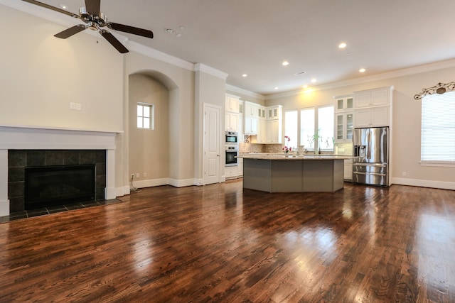 kitchen featuring appliances with stainless steel finishes, light stone counters, a kitchen island, a tiled fireplace, and ceiling fan