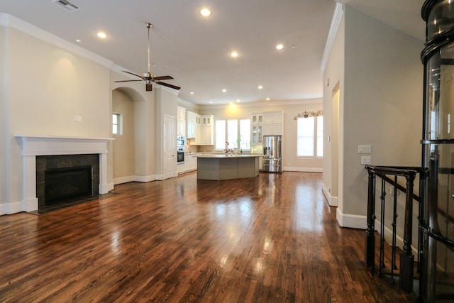 unfurnished living room with dark hardwood / wood-style floors, sink, a tiled fireplace, ornamental molding, and ceiling fan