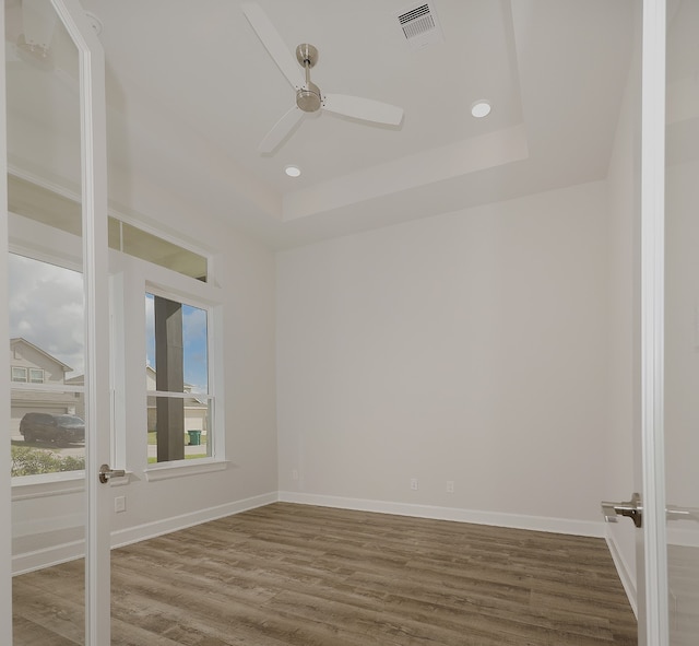 empty room with hardwood / wood-style floors, a tray ceiling, and ceiling fan