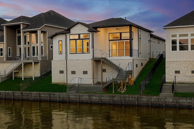 back house at dusk with a water view and a lawn