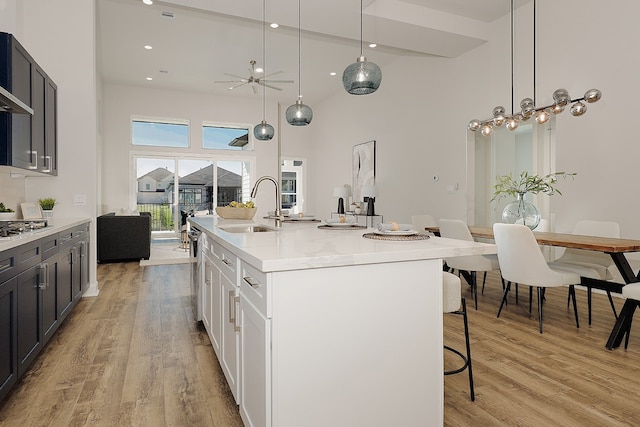 kitchen with sink, a towering ceiling, light hardwood / wood-style floors, a center island with sink, and white cabinets