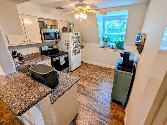 kitchen with appliances with stainless steel finishes, white cabinetry, ceiling fan, hardwood / wood-style flooring, and dark stone counters