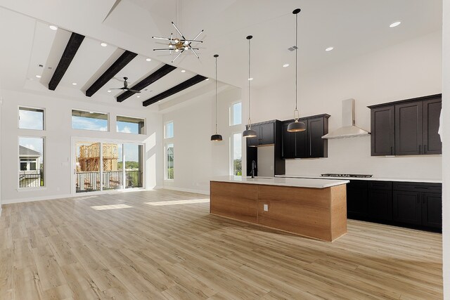 kitchen with a large island, pendant lighting, a high ceiling, wall chimney exhaust hood, and light hardwood / wood-style flooring