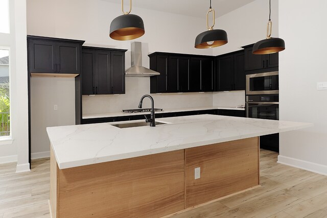 kitchen featuring wall chimney exhaust hood, a center island with sink, and decorative light fixtures