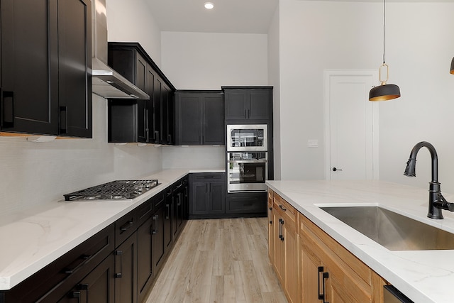 kitchen featuring light stone counters, wall chimney exhaust hood, light hardwood / wood-style flooring, sink, and appliances with stainless steel finishes