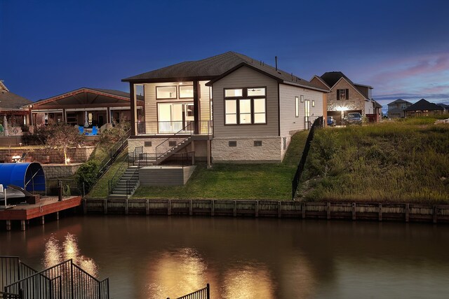 back house at dusk with a yard and a water view