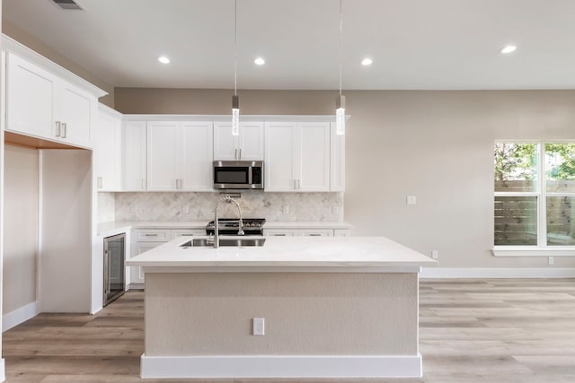 kitchen featuring white cabinets, an island with sink, hanging light fixtures, and sink