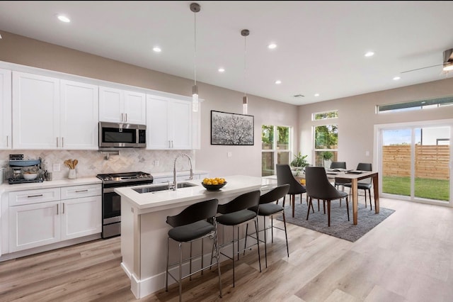 kitchen with light hardwood / wood-style floors, white cabinetry, an island with sink, pendant lighting, and stainless steel appliances