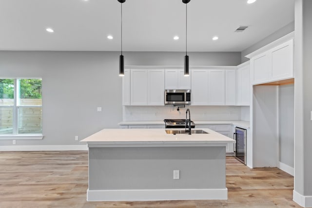 kitchen featuring an island with sink, sink, light hardwood / wood-style flooring, decorative light fixtures, and white cabinetry