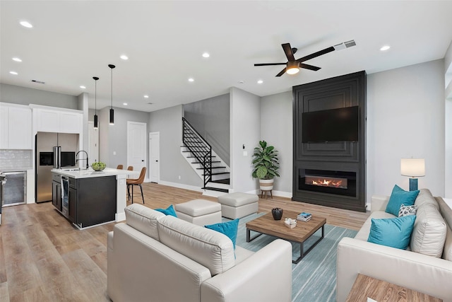 living room with light hardwood / wood-style floors, a large fireplace, ceiling fan, and sink