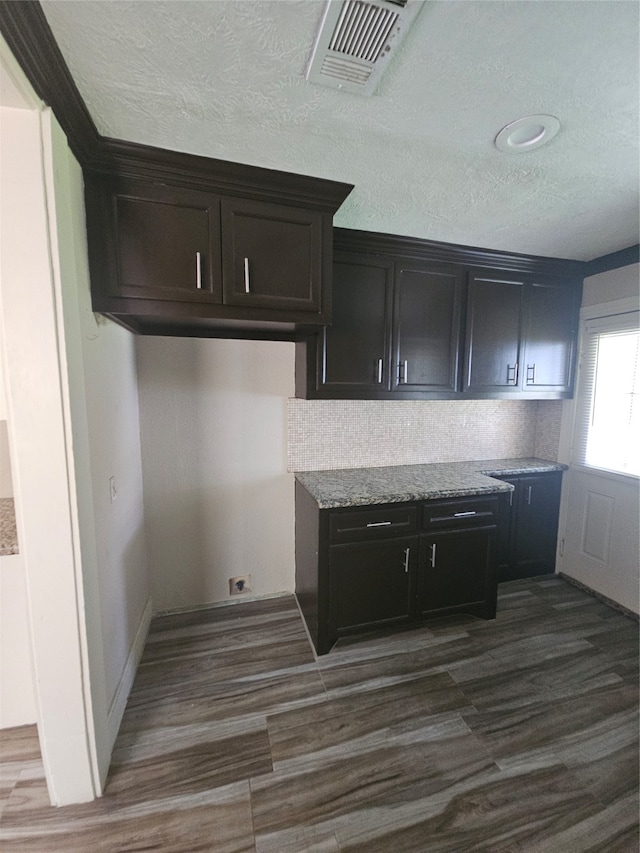 kitchen with light stone countertops, dark brown cabinetry, dark wood-type flooring, and tasteful backsplash