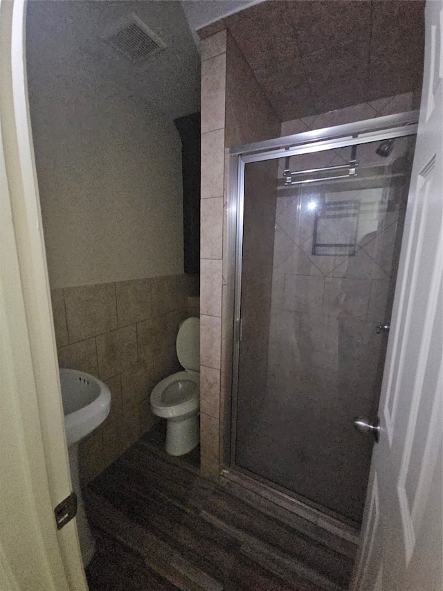 bathroom featuring tile walls, hardwood / wood-style flooring, a shower with door, and toilet