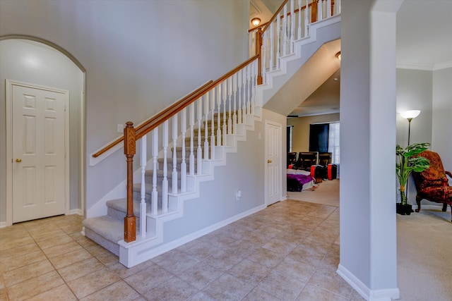 staircase featuring crown molding, carpet flooring, and a high ceiling