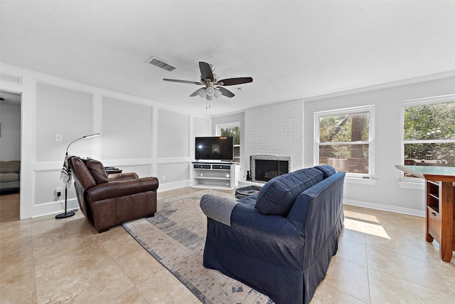 living room featuring light tile patterned floors, ceiling fan, a fireplace, and a textured ceiling