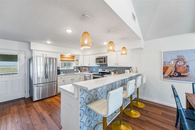 kitchen with kitchen peninsula, decorative light fixtures, white cabinetry, stainless steel appliances, and dark hardwood / wood-style flooring