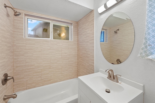 bathroom with a textured ceiling, tiled shower / bath combo, and vanity