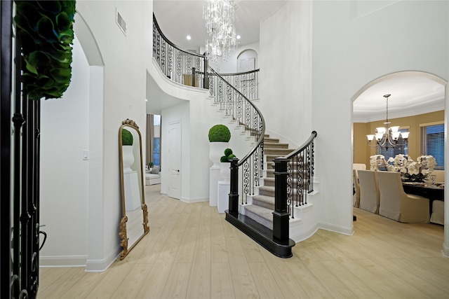 entrance foyer featuring an inviting chandelier, a towering ceiling, light hardwood / wood-style floors, and crown molding