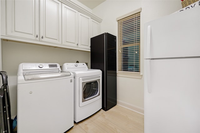 clothes washing area with separate washer and dryer, cabinets, and light wood-type flooring