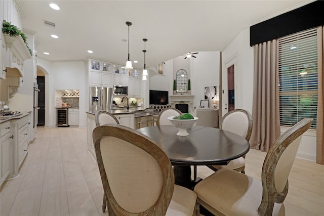 dining room featuring wine cooler, crown molding, ceiling fan, light hardwood / wood-style flooring, and sink