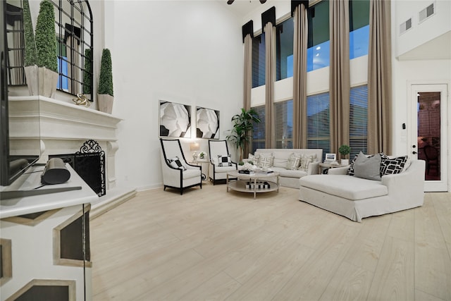 living room featuring a towering ceiling, a high end fireplace, and light wood-type flooring