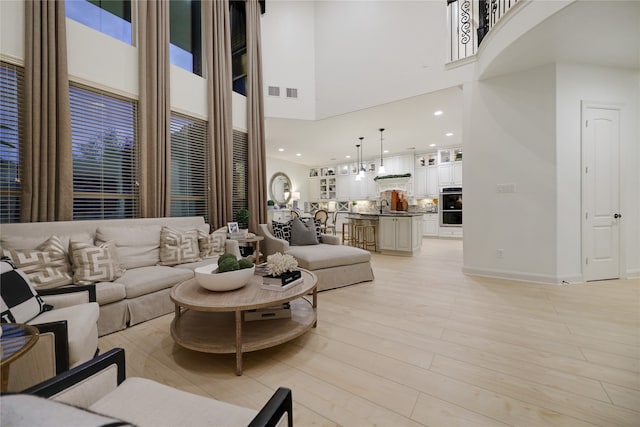 living room featuring a high ceiling, light wood-type flooring, and sink