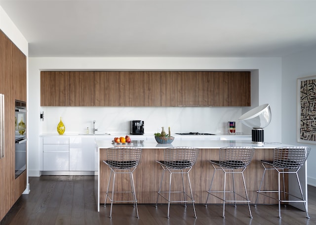 kitchen featuring dark wood-type flooring, a breakfast bar area, white gas stovetop, oven, and sink