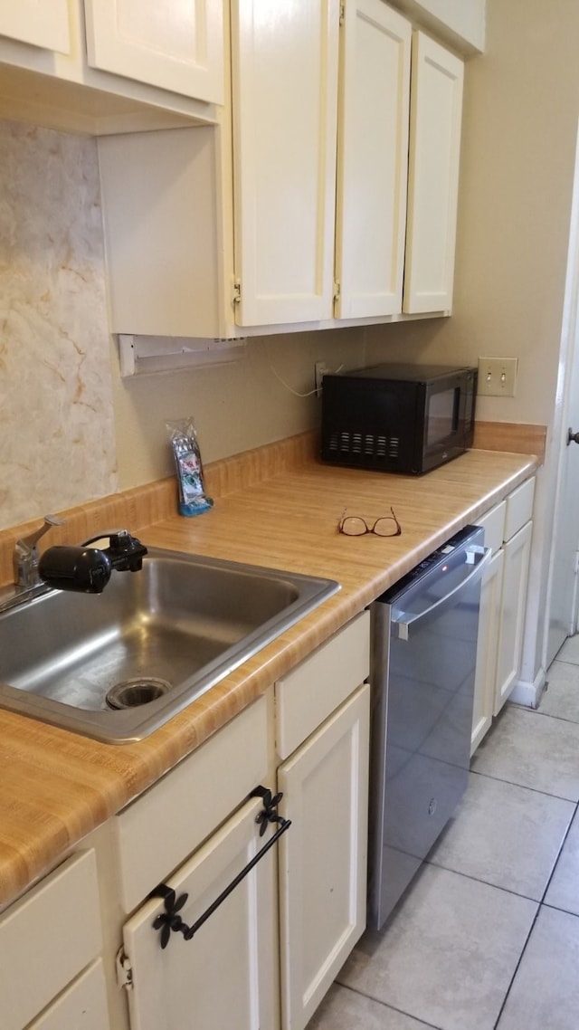 kitchen featuring white cabinetry, sink, light tile patterned floors, and stainless steel dishwasher