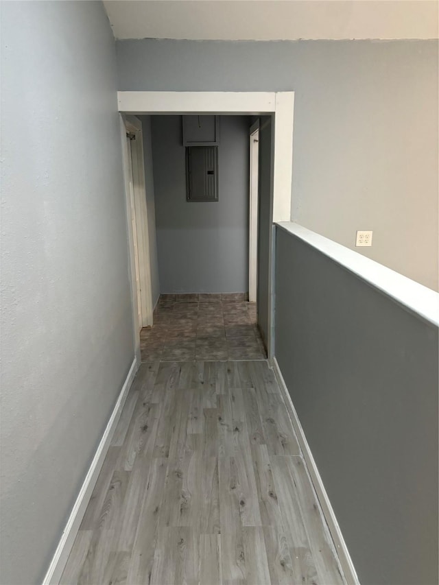 hall with light wood-type flooring, electric panel, and baseboards