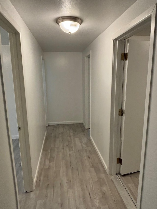 corridor featuring light wood-type flooring and baseboards