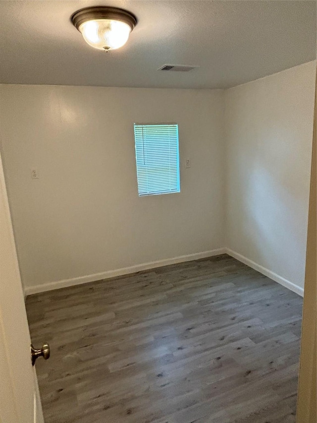 unfurnished room featuring baseboards, visible vents, and wood finished floors