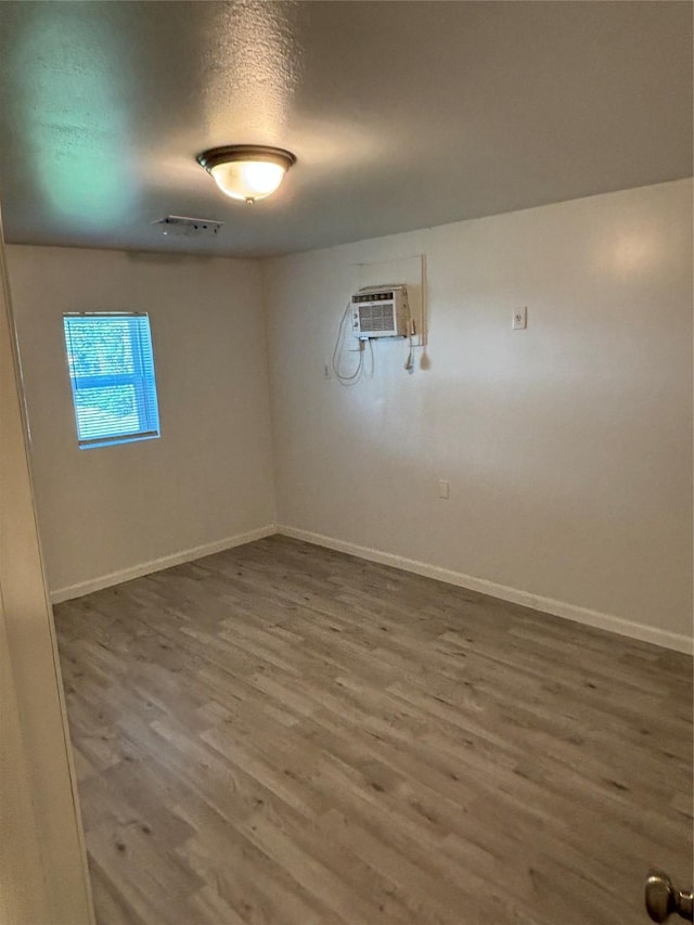 unfurnished room featuring a wall mounted air conditioner, visible vents, baseboards, and wood finished floors