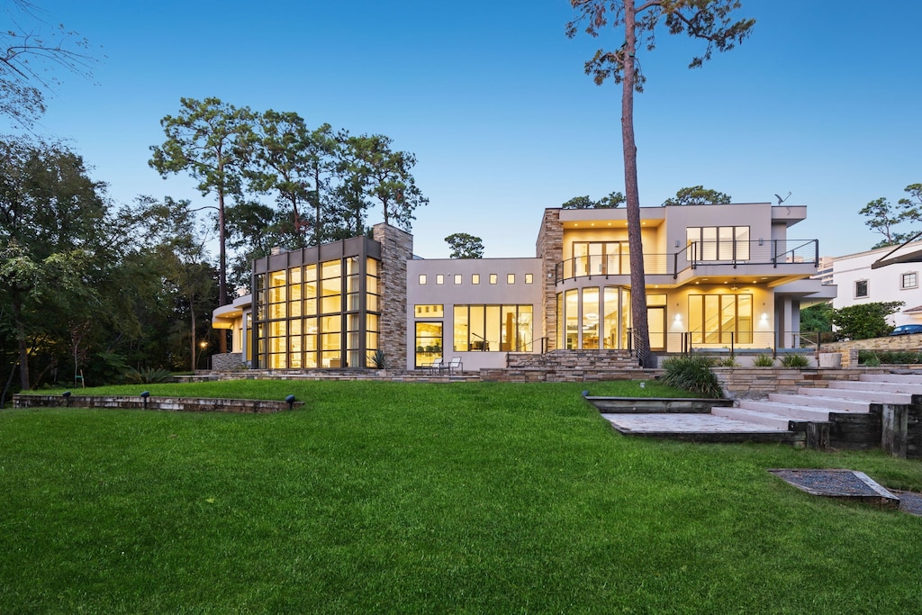 back house at dusk featuring a balcony and a lawn