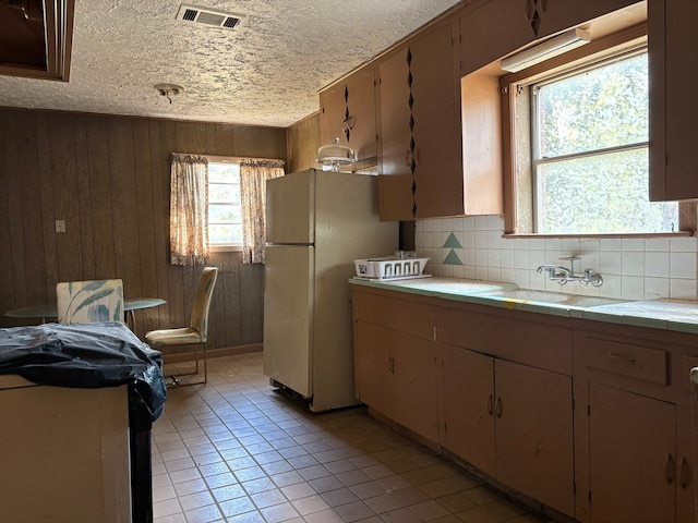 kitchen with wood walls, a textured ceiling, backsplash, tile countertops, and white fridge