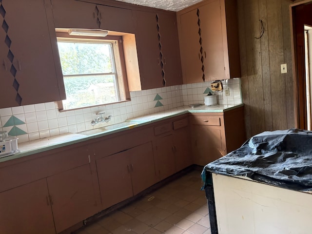 kitchen featuring decorative backsplash, wood walls, light tile patterned floors, and sink