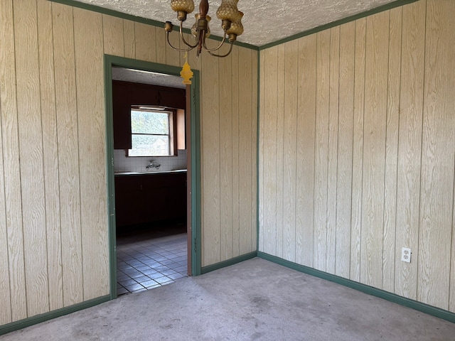 spare room with an inviting chandelier, wood walls, and a textured ceiling