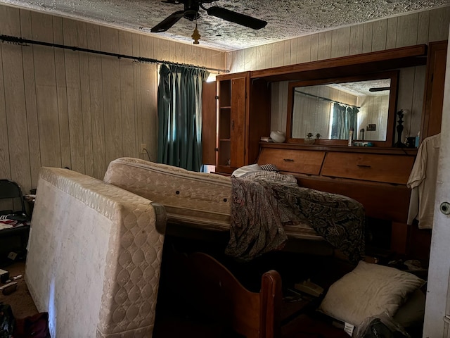 bedroom with a textured ceiling, wood walls, and ceiling fan