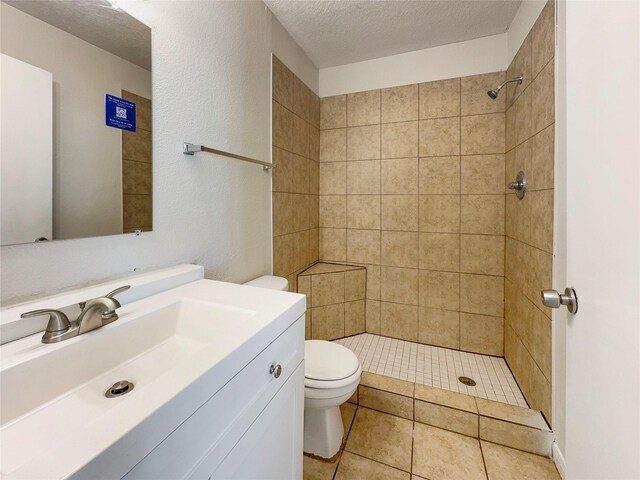 bathroom with a tile shower, tile patterned flooring, a textured ceiling, vanity, and toilet