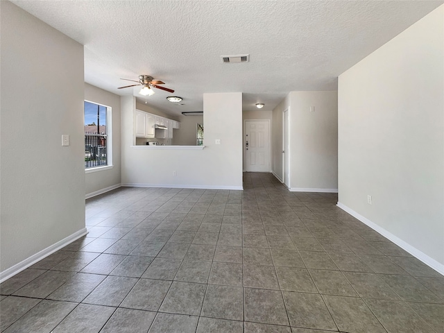 unfurnished living room with a textured ceiling, ceiling fan, and dark tile patterned floors