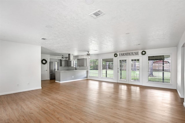 unfurnished living room with light hardwood / wood-style floors, ceiling fan, and a textured ceiling