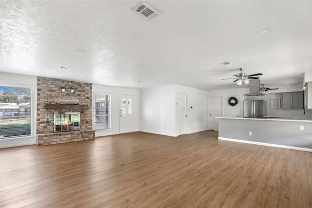 unfurnished living room with a brick fireplace, a textured ceiling, ceiling fan, and dark hardwood / wood-style floors