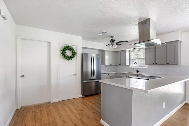 kitchen featuring kitchen peninsula, light hardwood / wood-style floors, island exhaust hood, black electric stovetop, and stainless steel refrigerator