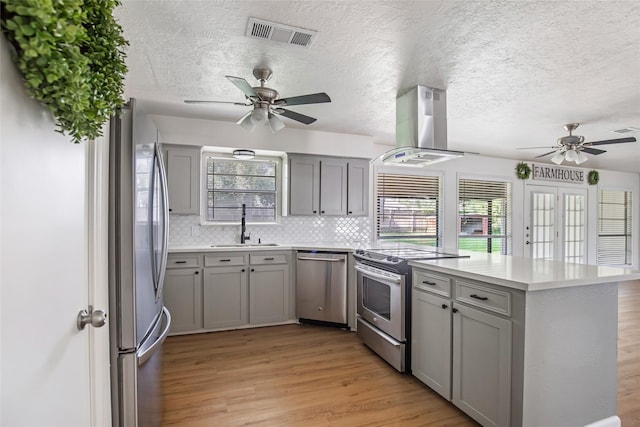 kitchen featuring stainless steel appliances, sink, light hardwood / wood-style flooring, kitchen peninsula, and island range hood