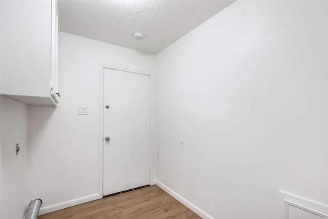 laundry area featuring electric dryer hookup, a textured ceiling, cabinets, and light hardwood / wood-style flooring