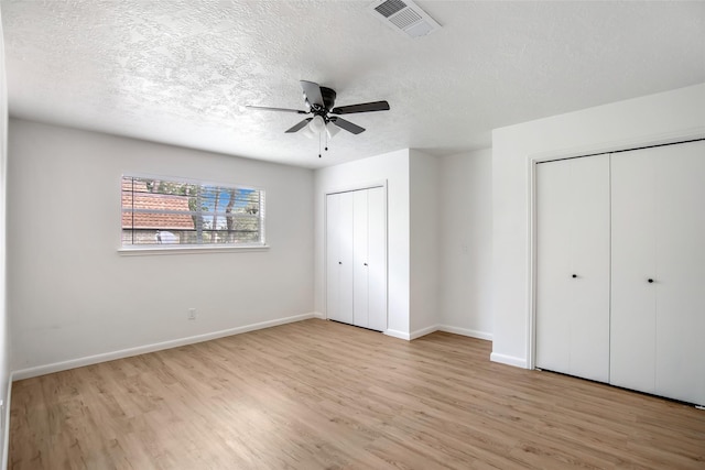 unfurnished bedroom with light wood-type flooring, two closets, and ceiling fan